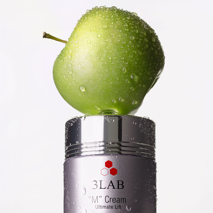 Dewy green Swiss apple resting on a jar of 3LAB "M" Cream, the source of its apple stem cell technology